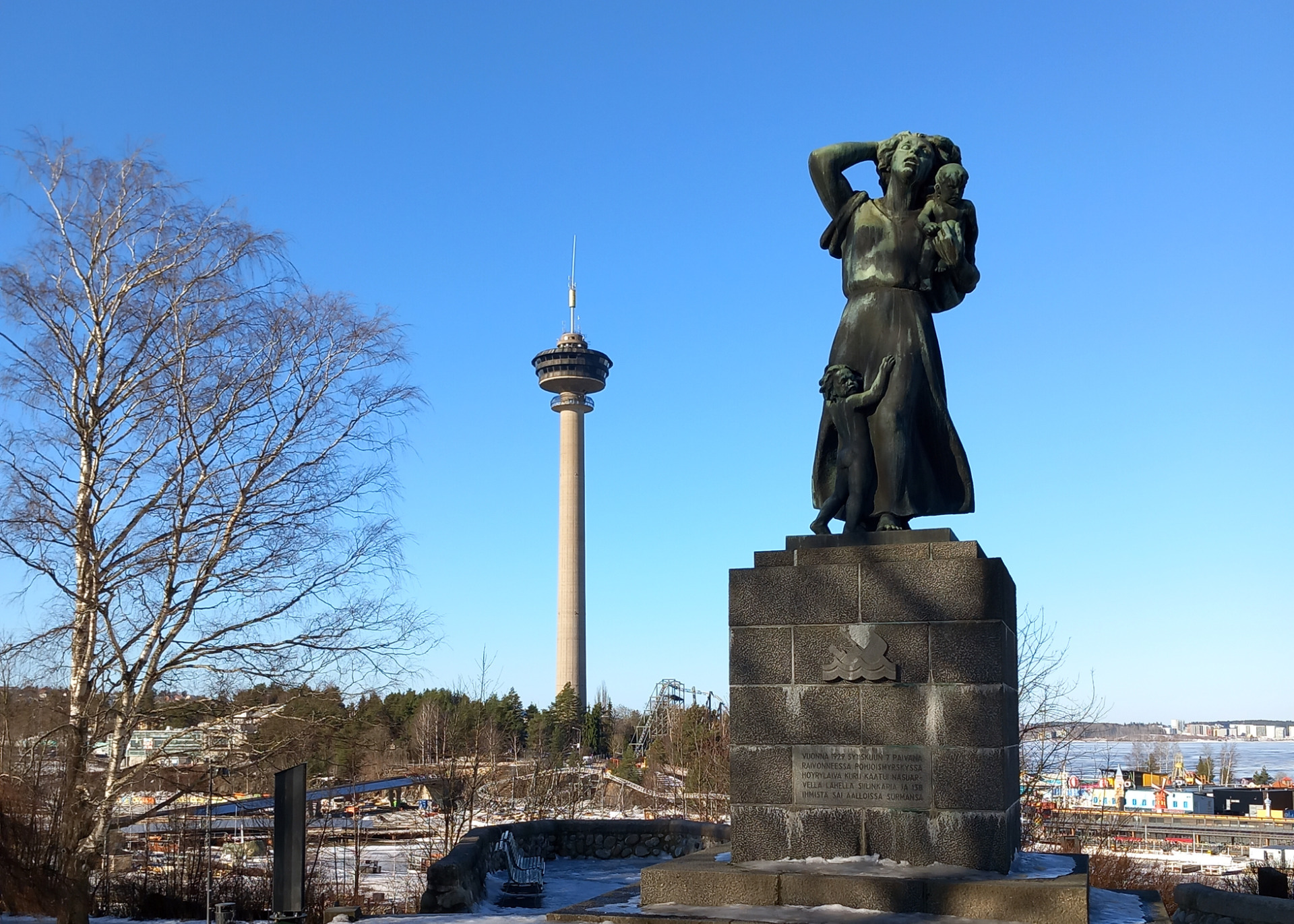 Pronssinen patsas kohottaa kätensä, taustalla sininen taivas ja Näsinneula.